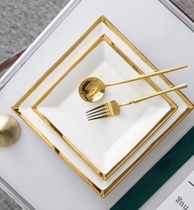 Detailed view of white ceramic square plates with gold trim and matching gold cutlery