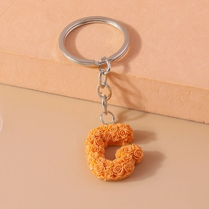 Detail of letter G keychain featuring orange-pink resin roses and silver metal ring