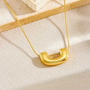 Minimalist gold plated stainless steel U-shape pendant necklace on a beige textured stone