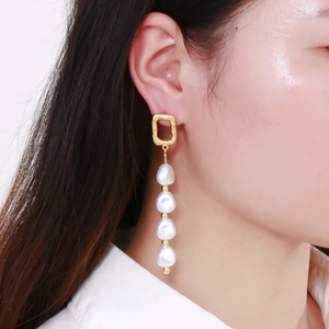 Gros plan de boucles d'oreilles pendantes en perles baroques et clous géométriques dorés
