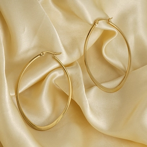 Macro detail of gold-plated teardrop hoop earrings on champagne silk fabric background