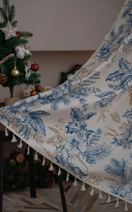 Detail of Christmas tablecloth with blue pine motifs, gold leaves, and white fringe