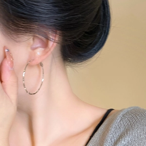 Close-up of model wearing large silver textured hoop earrings on a beige background
