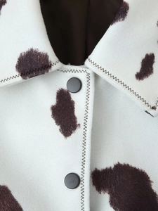 Detail of cream jacket with cow print featuring black buttons and zig-zag stitching