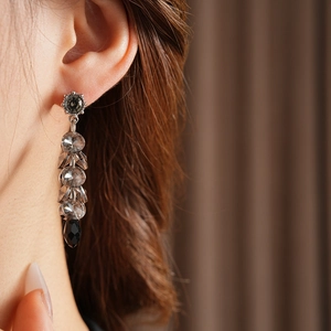 Detailed view of silver needle drop earrings with sparkling black and clear tassels on model