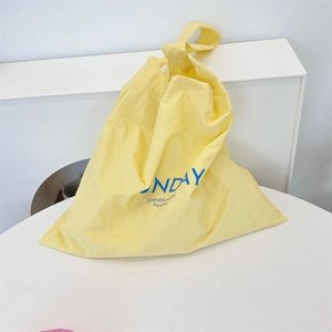 Detail of light yellow canvas tote bag with blue SUNDAY print on a minimal background