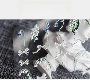 Détail de stickers 3D pour ongles avec motifs de muguet et nœuds blancs élégants