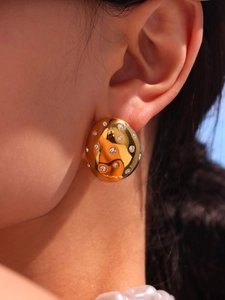 Detailed close-up of a model wearing a gold oval earring with sparkling crystals