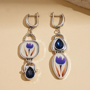Détail de boucles d'oreilles asymétriques argentées avec pierres bleues et émail tulipe