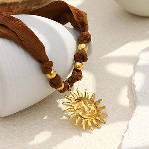 Macro view of sun face pendant necklace with brown silk cord and gold beads