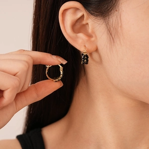 Detailed view of wheat-shaped earrings with gold base and black stones on a hand