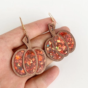 Halloween pumpkin earrings with orange glitter sequins and natural wood frame held in hand
