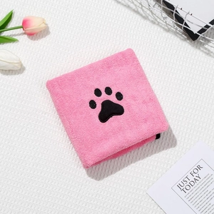 Detail of pink microfiber pet towel with black paw print embroidery on grid background