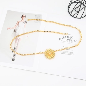 Detail of a golden sunflower pendant on a textured box chain draped over a magazine