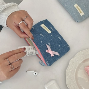 Dettaglio del portamonete in denim blu con ricamo a fiocco rosa e chiusura a zip pratica
