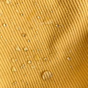 Close-up of waterproof yellow corduroy fabric showing detailed texture and water beads