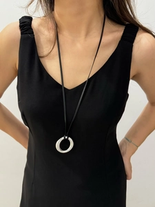 Minimalist silver circle pendant on black leather cord shown worn on a black dress