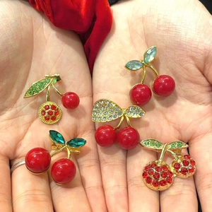 Cute cherry and bow brooches set with red pearls and crystals on hand display