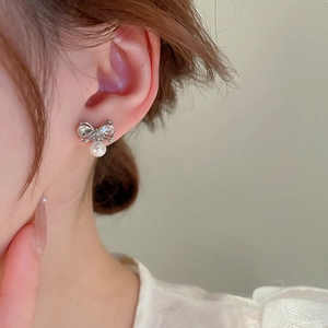 Close-up of elegant bow-knot pearl earrings with sparkling diamonds on a model