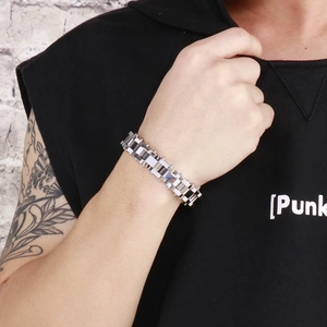 Silbernes Herrenarmband im Punk-Stil an tätowiertem Model vor einer Ziegelmauer-Kulisse