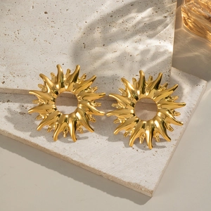 Detail of golden sunburst stud earrings on beige stone showing polished texture