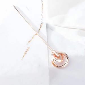 Detail of rose gold metal hair pin with interlocking circles on marble texture background