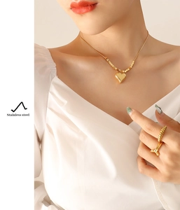 Close-up of golden stainless steel heart pendant necklace and textured rings on model