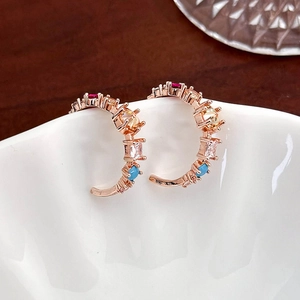Close-up of rose gold C-shaped earrings with colorful zircons on white porcelain