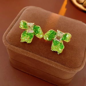 Close-up of gold-plated clover earrings with green stones on a velvet jewelry box