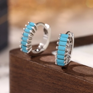 Macro view of silver square earrings with turquoise stones on dark wood