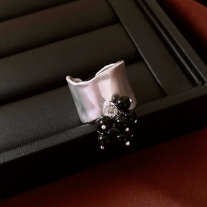 Macro shot of wide irregular silver wavy ring with hanging black beaded charms on leather