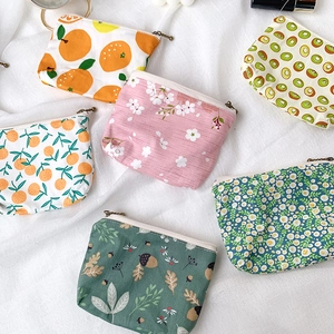 Close-up of mini canvas wallets with fruit and floral prints on white fabric