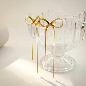 Detail view of gold bow knot tassel earrings hanging on the edge of a crystal glass