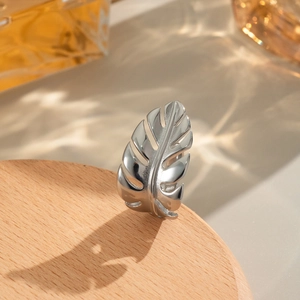 Macro view of silver monstera leaf ring on wooden base with aesthetic lighting shadows