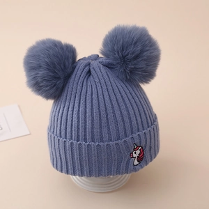 Detail of baby unicorn knit hat with sky blue ribbed texture and faux fur double pom-poms