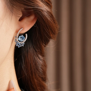 Close-up of a silver U-shaped earring with hexagonal blue zircon on a model's ear