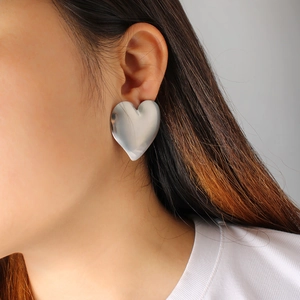 Close-up of polished silver heart-shaped hoop earrings worn by a model in soft light