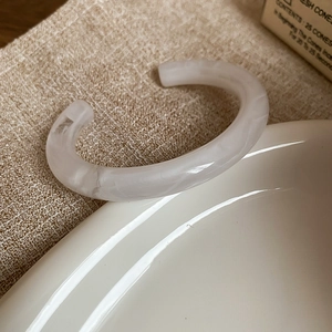 Detailed close-up of cream-white marble texture resin open bangle on a ceramic plate