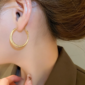 Gros plan de boucles d'oreilles créoles dorées mates sur l'oreille d'un mannequin