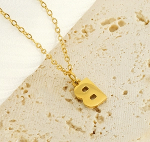 Macro view of gold letter B necklace on beige travertine stone with silk detail