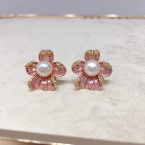 Macro shot of 18K gold flower earrings with pink enamel petals and a central white pearl