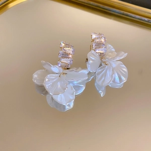 Macro shot of white floral petal earrings with rectangular crystals on a gold mirror tray