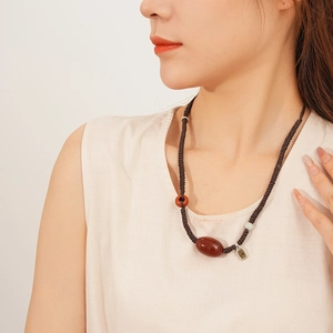 Detail of red agate pendant necklace with woven cord on a model in soft lighting