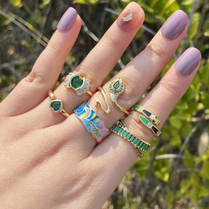 Detail of gold snake and wing rings set with green stones on a model hand