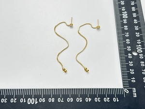 Detailansicht langer goldener Kettenohrringe mit Kristallsteckern neben einem Lineal