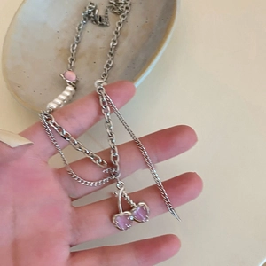 Close-up of layered necklace with pink cherry pendant and pearls held in hand