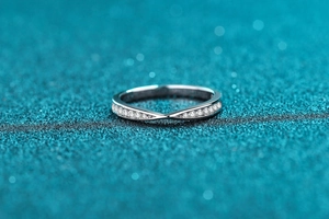 Macro detail of V-shaped S925 silver cross ring with pavé moissanite stones on blue texture