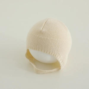 Dettaglio della trama a maglia di un cappellino crema per neonati con lacci