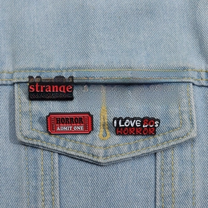 Set of 5 horror movie enamel pins on denim jacket featuring creepy movie quotes and icons