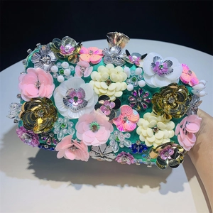 Detailed close-up of 3D sequin flowers and crystal beads on a green satin evening bag